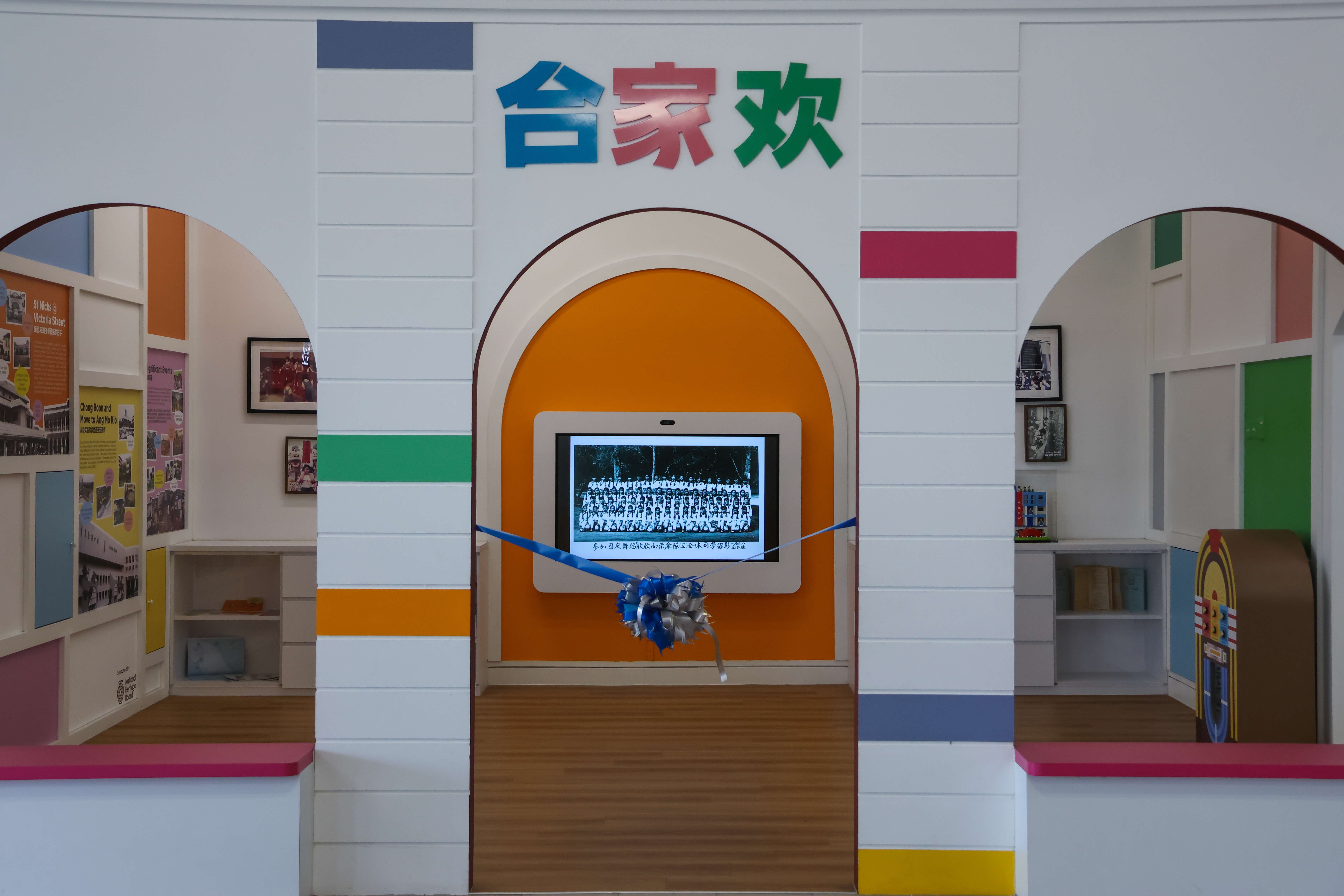 A colourful heritage exhibition display featuring the Chinese characters '合家欢' (meaning 'family reunion' or 'whole family joy') in blue, red, and green at the top. 
